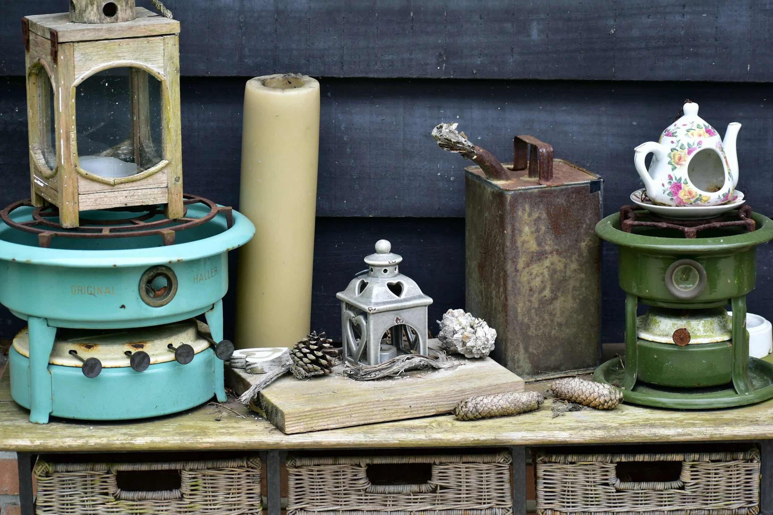 Collection of vintage household items including a turquoise stove, candles, a teapot, pine cones, and decorative objects on a wooden surface.