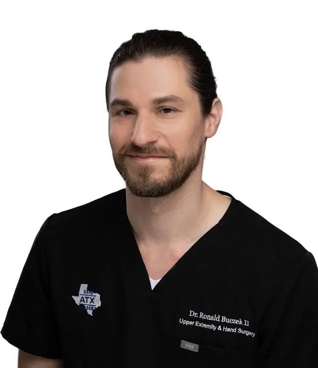 Portrait of a man with beard and mustache wearing black medical scrubs, smiling slightly against a white background.