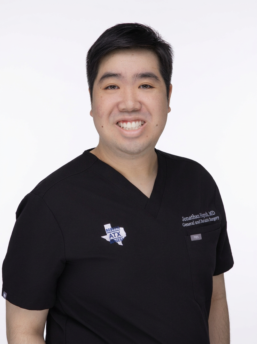 A man with short black hair, smiling, wearing black medical scrubs with an 'ATX Surgery' logo on the chest, standing against a plain white background.