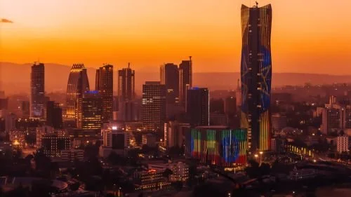 Sunset over a city skyline with tall skyscrapers and colorful lights.