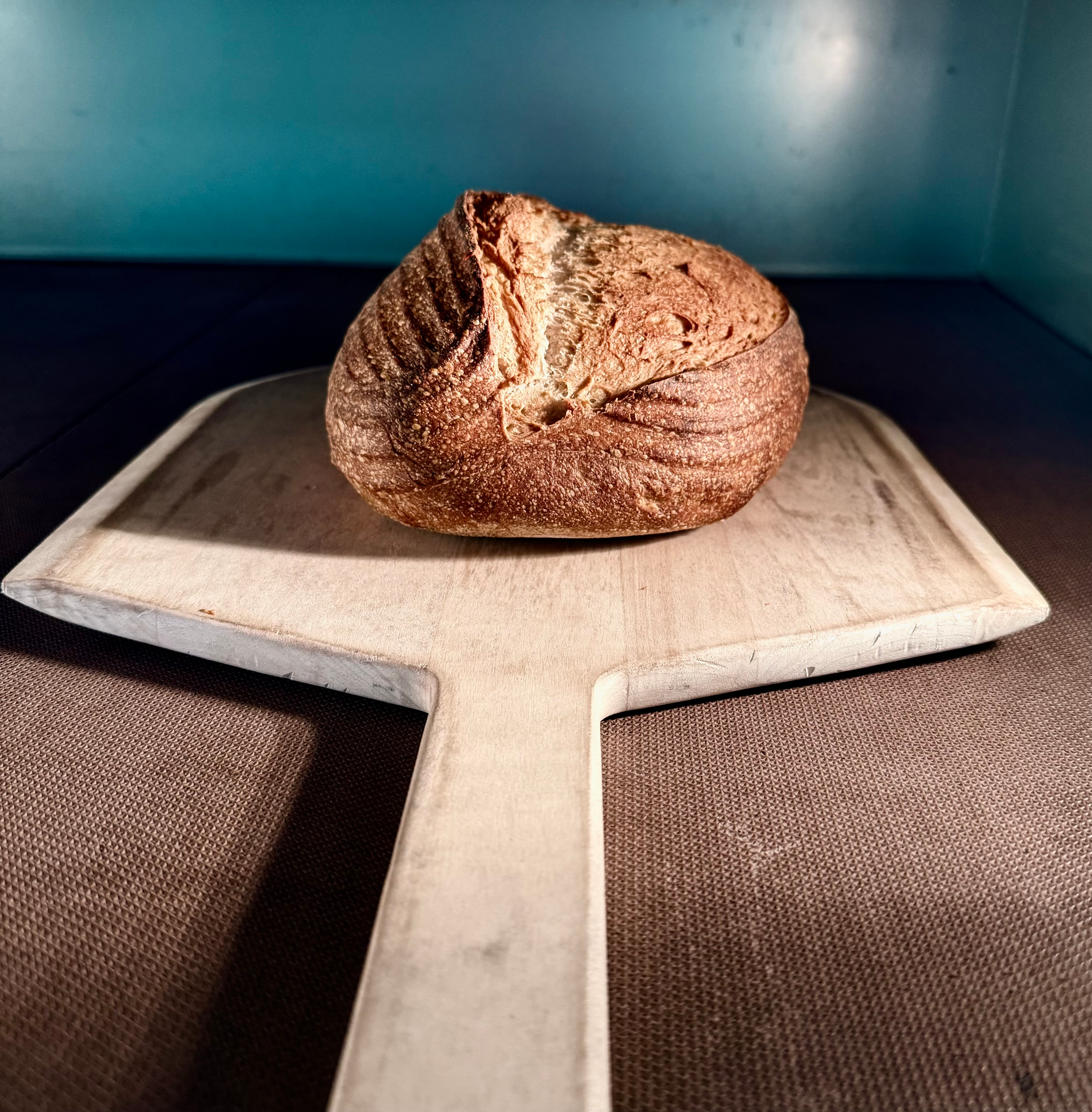 Close-up image of a rustic round bread loaf with a cracked crust, placed on a wooden cutting board.
