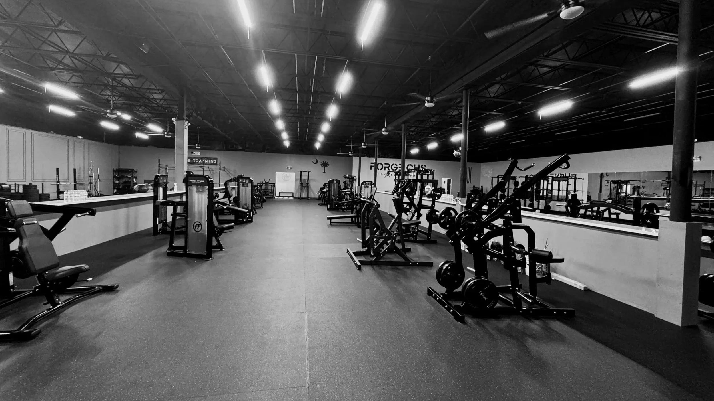FORGE CHS exercise equipment including weights, cardio machines, and strength training equipment, illuminated by overhead lighting.