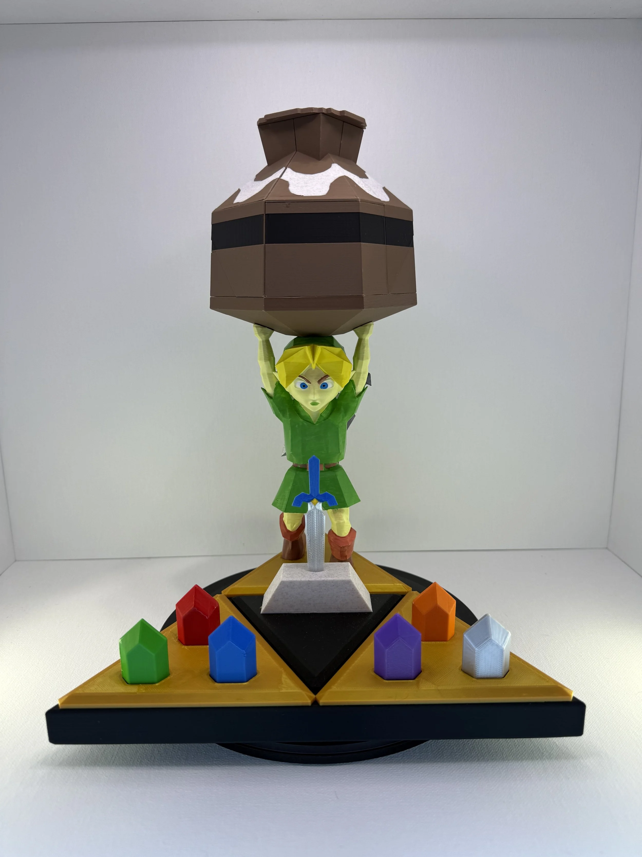 A 3D-printed elf-warrior statue standing on a triangular display base, holding up a large brown hexagonal jar puzzle with white accents, surrounded by colorful gem-shaped pieces.