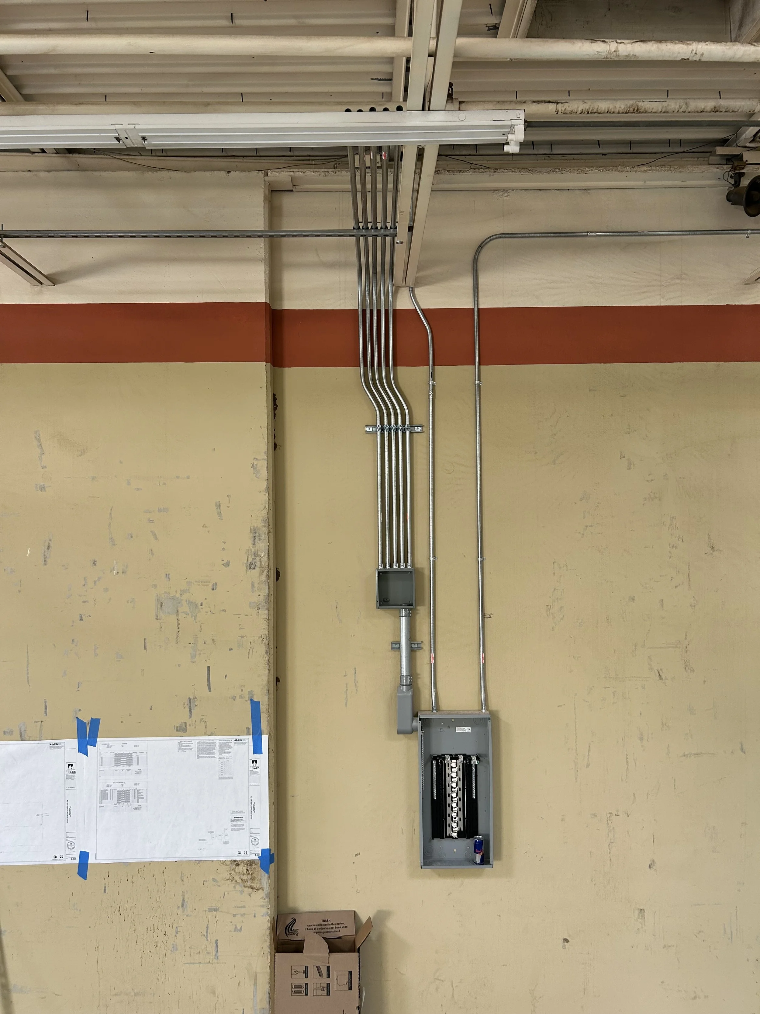 Electrical wiring and conduit mounted on a yellow wall in an industrial or warehouse setting.