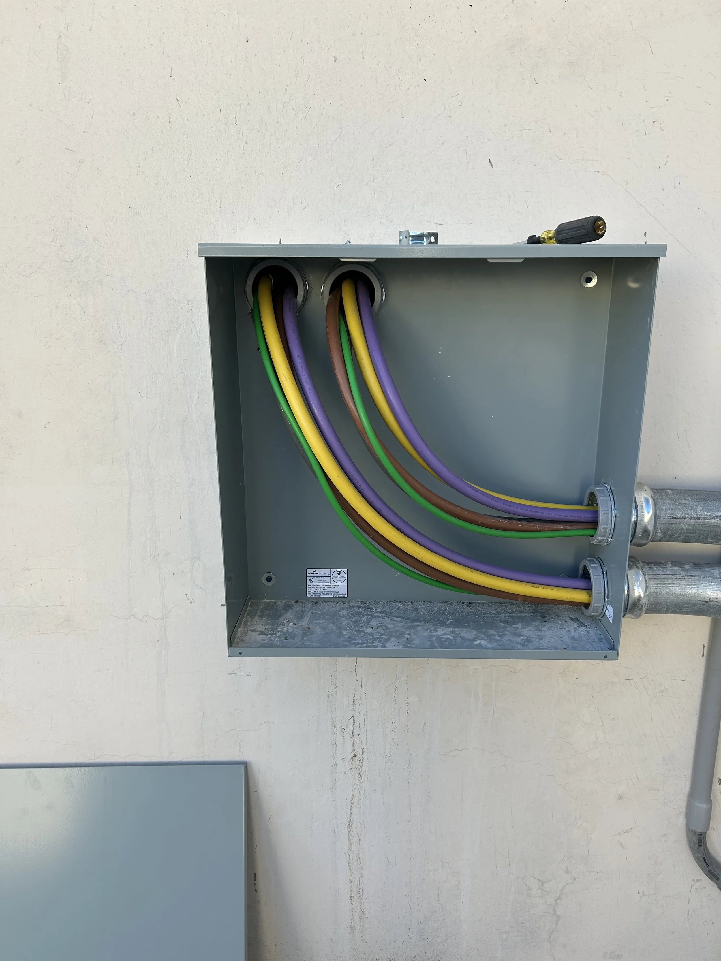 Electrical box with colorful wiring, including yellow, purple, brown, and green wires, on a beige wall.