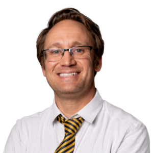 A smiling man with glasses, wearing a white shirt and yellow striped tie, against a plain white background.