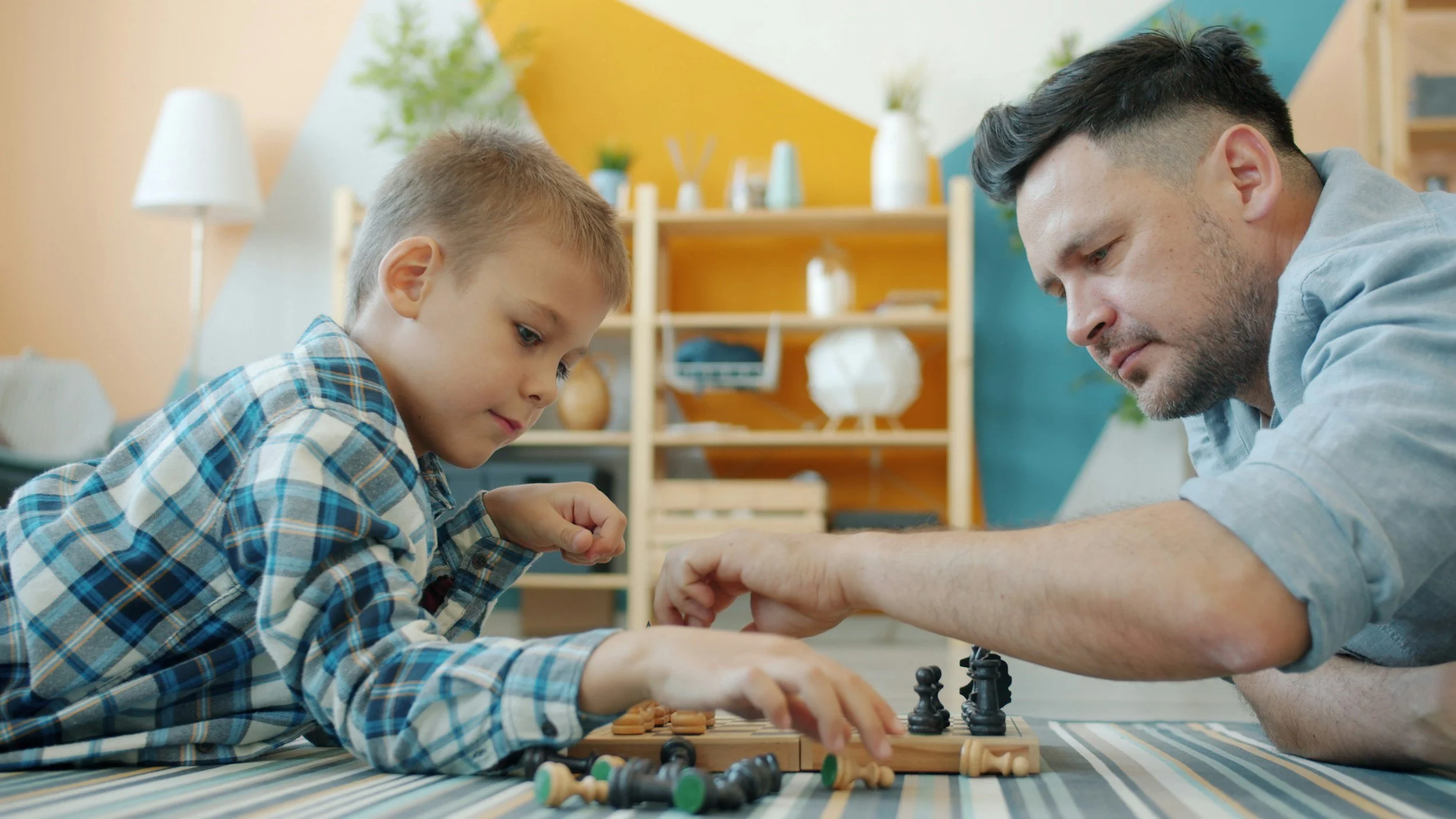 A young boy and an adult man playing chess together at a table in a brightly decorated room.