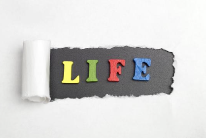 Colorful foam letters spelling 'LIFE' on a gray torn paper background.