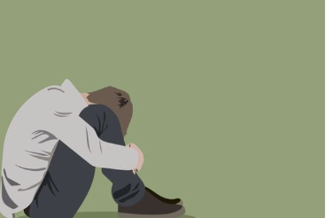 A person sitting on the floor with their head down and arms wrapped around their knees, against a light green background.