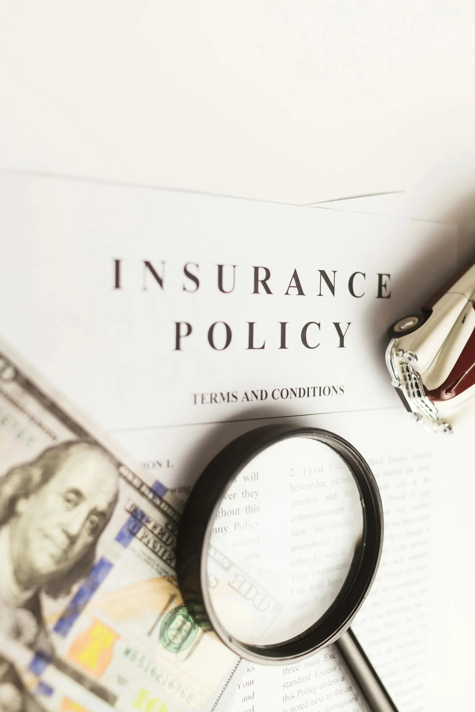 Insurance policy document with a magnifying glass and U.S. dollar bills on top.