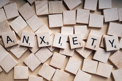 Wooden Scrabble tiles spelling the word 'ANXIETY' surrounded by plain wooden tiles.