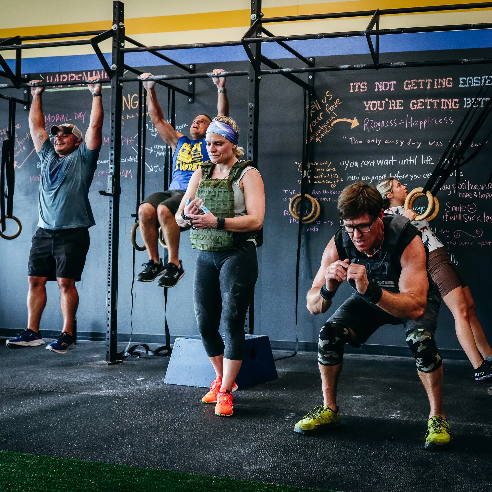 People working out in a gym, performing pull-ups on a squat rack. Join CFCA and workout with our community