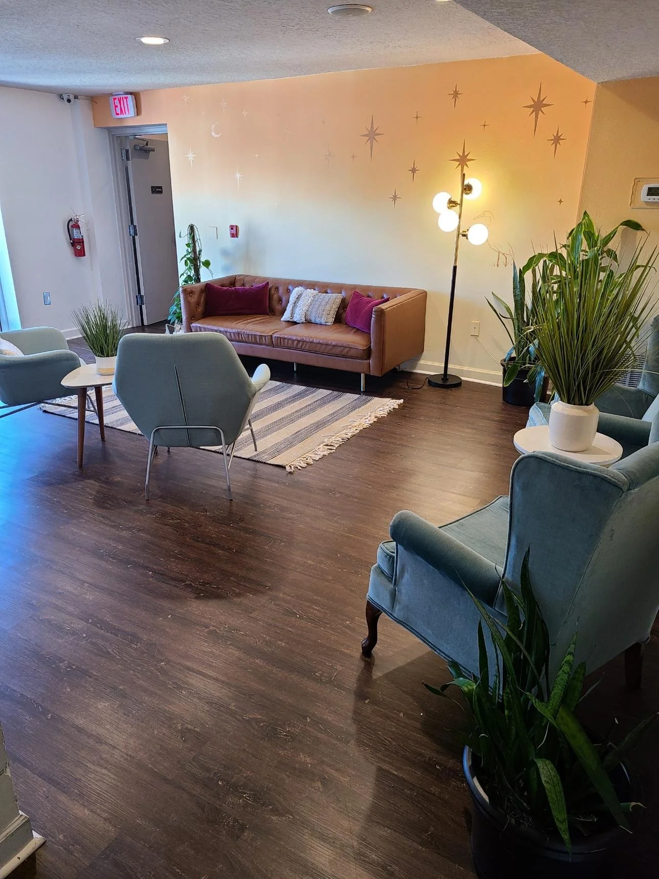 Stylish indoor living room with a leather sofa, armchairs, potted plants, a striped rug, and a modern floor lamp, with a starry wall decoration and wooden flooring.