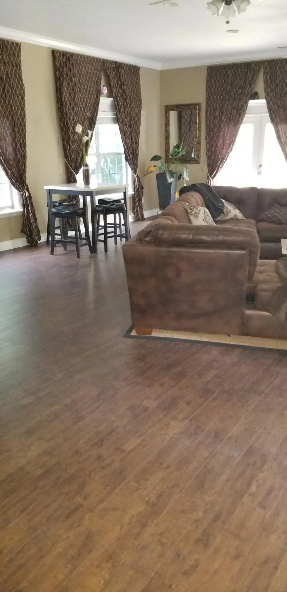 Living room with brown leather sectional sofa, dark wood flooring, and windows with diamond-patterned brown curtains.