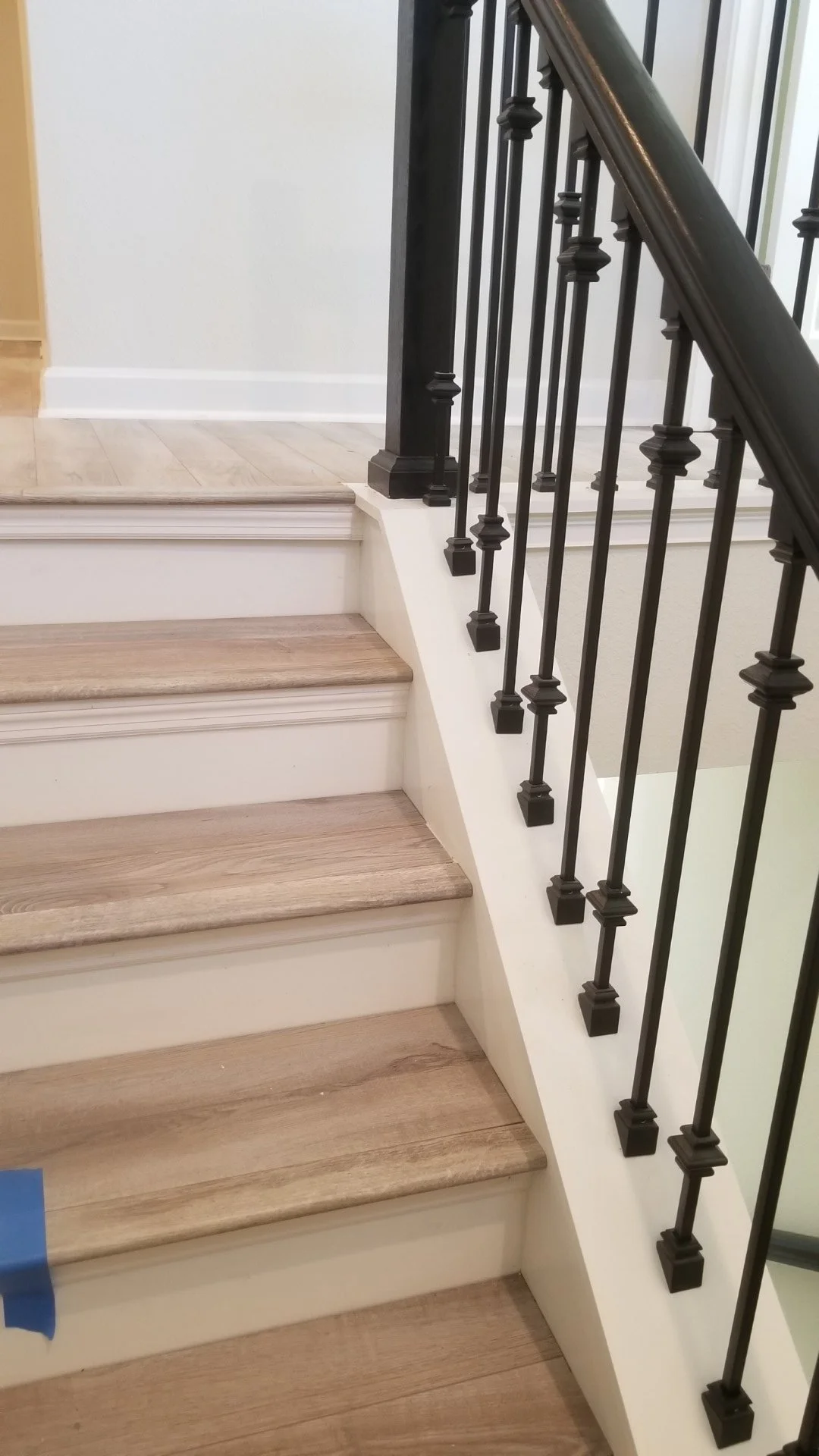 Wooden stairs with a white baseboard and a black metal railing leading up to a higher level, inside a house or building.