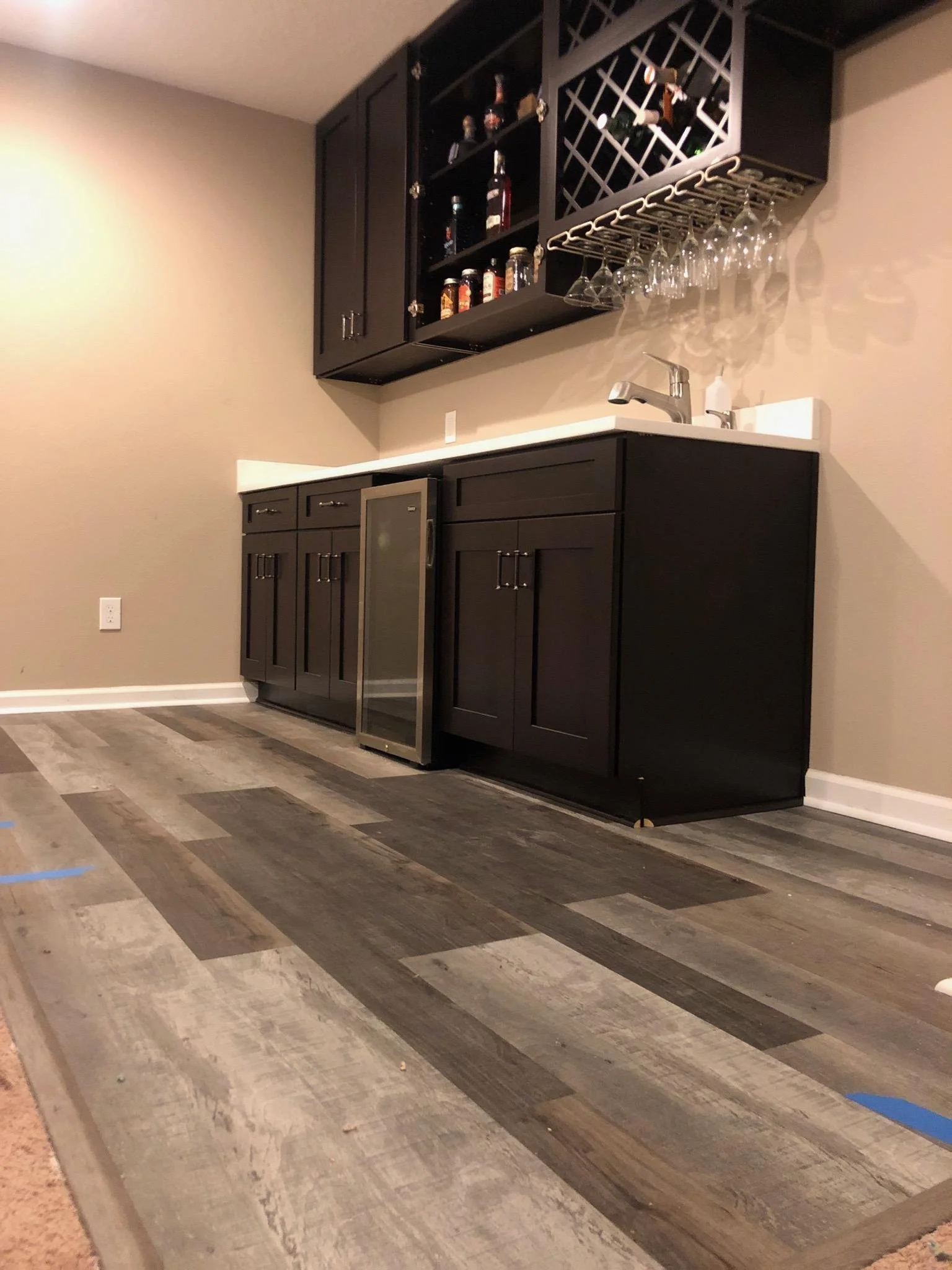 A bar area with black cabinets, a countertop with a sink, and a wooden floor with gray and brown planks.