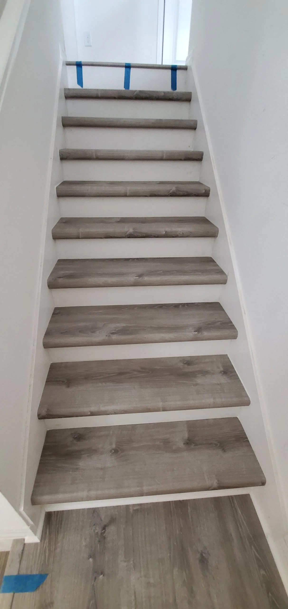 Wooden staircase with white risers and a blue tape at the top.