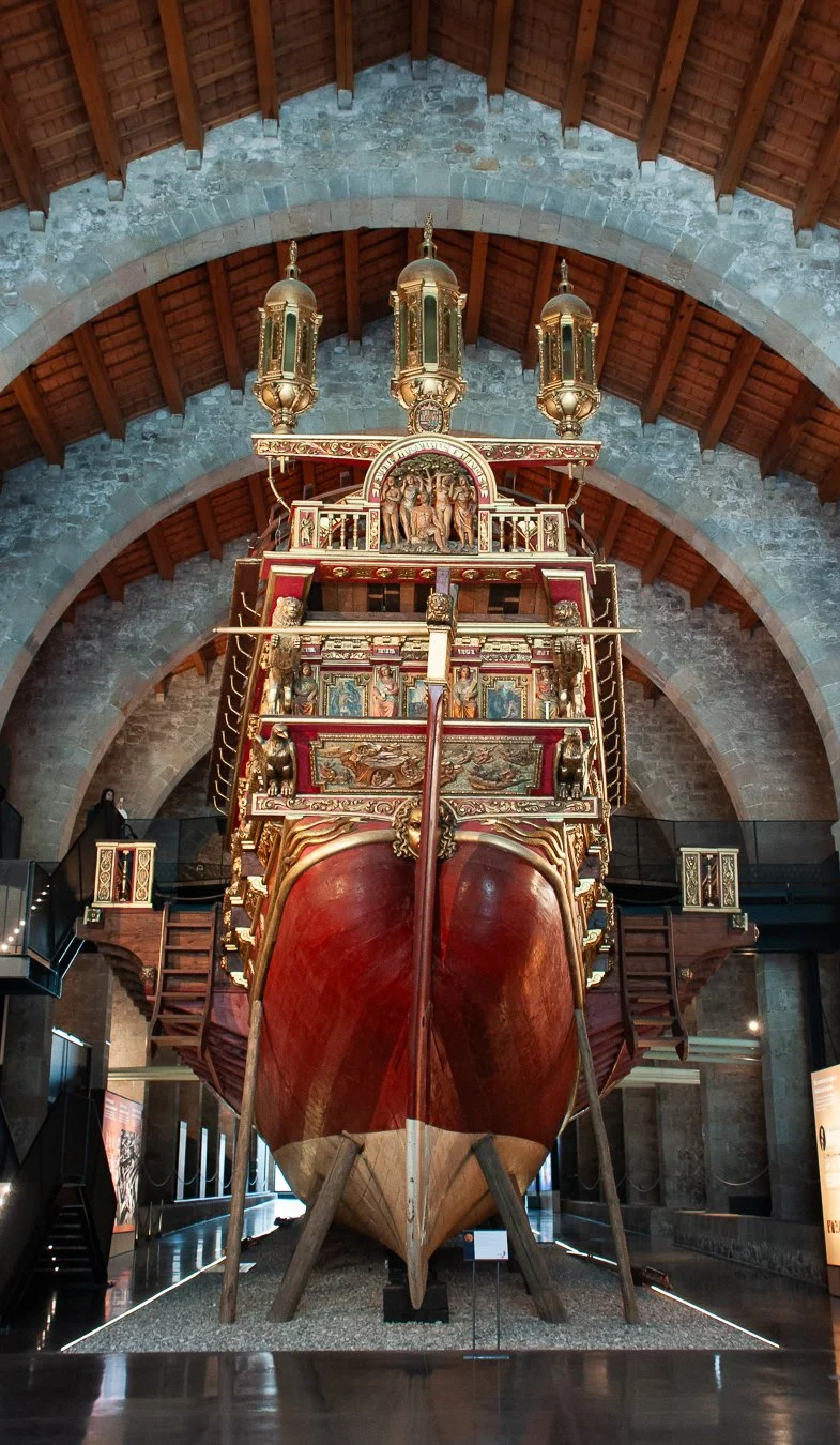 Historic wooden ship on display inside a museum with stone and wooden architecture.