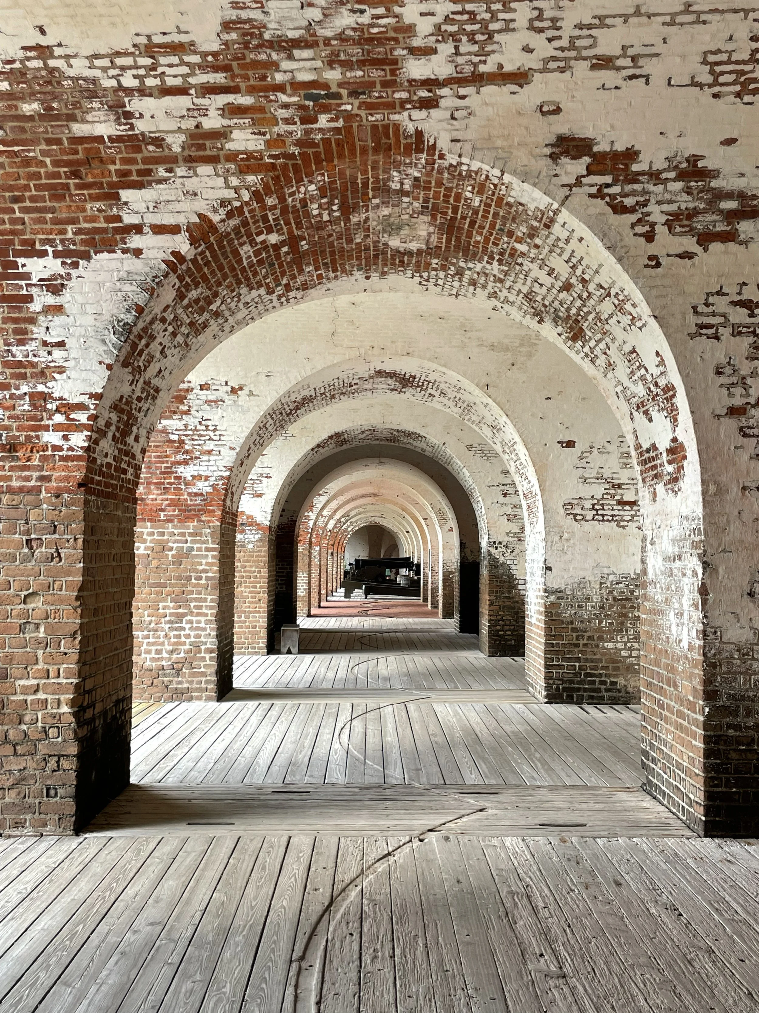 A long corridor with brick arches and a wooden floor, leading to a distant empty space.