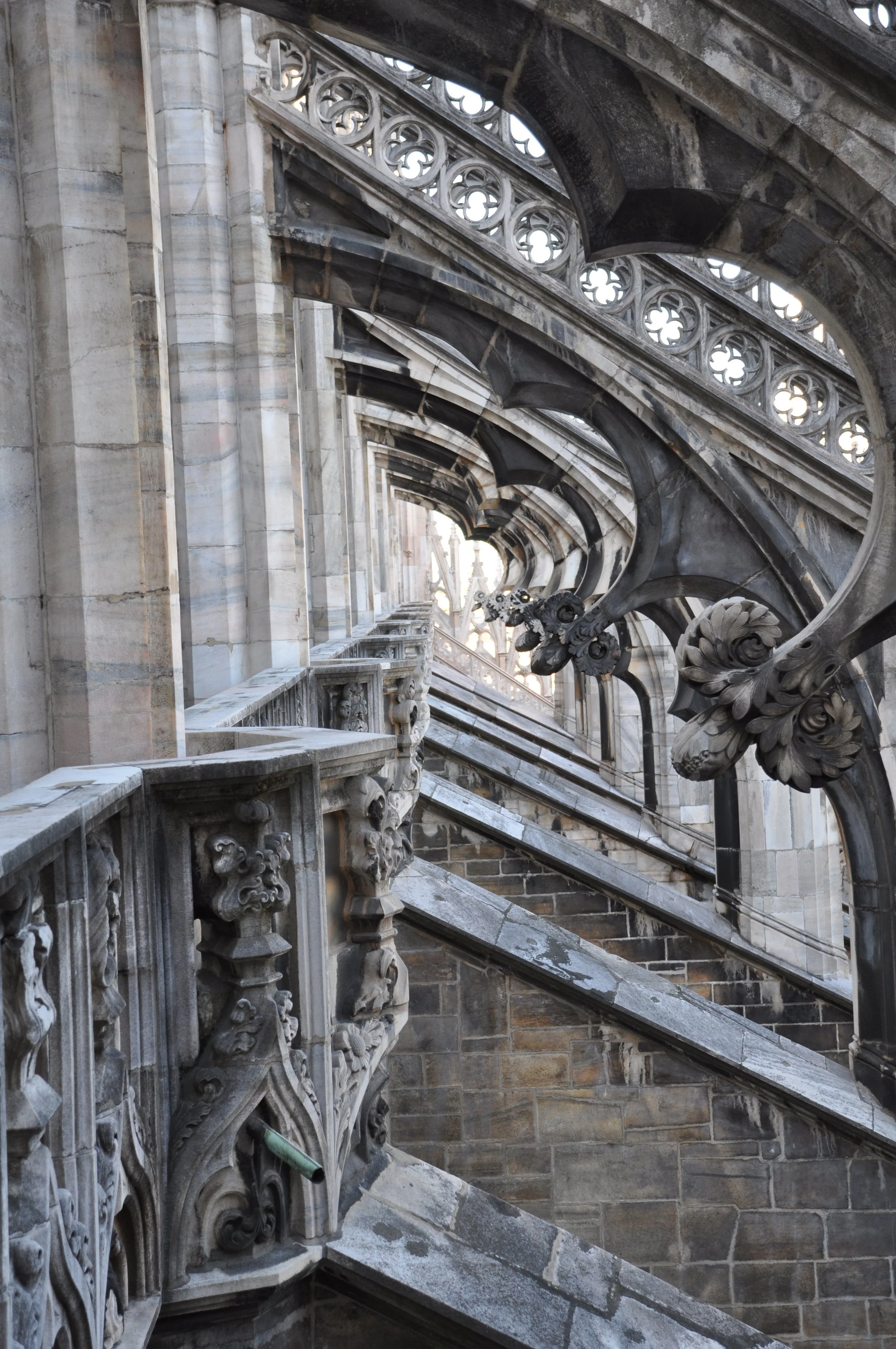 View of ornate stone and marble architectural details on an exterior building, featuring decorative balustrades, carved floral motifs, and arched elements.
