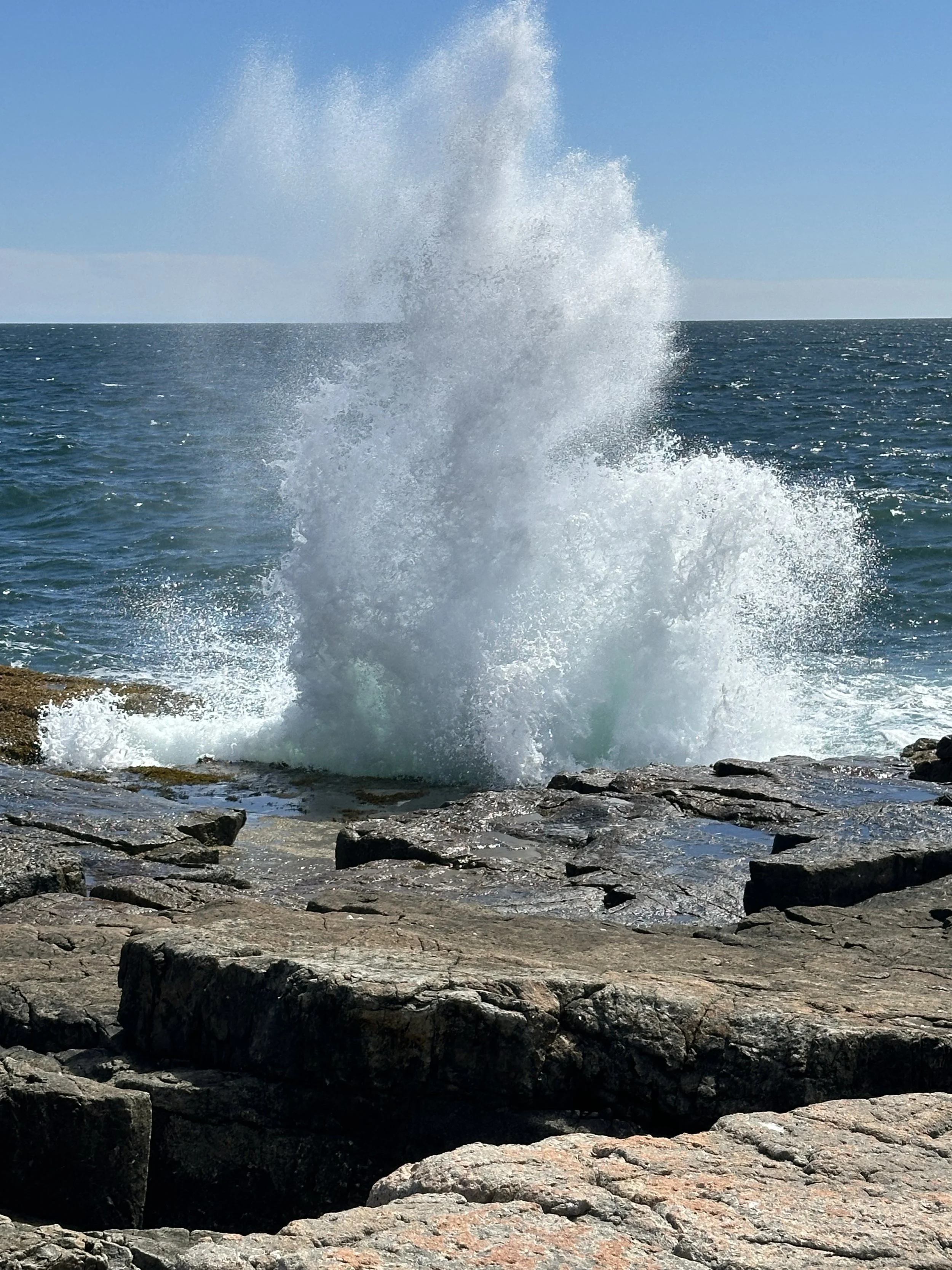 Ocean waves crashing against rocky shoreline under a clear blue sky.