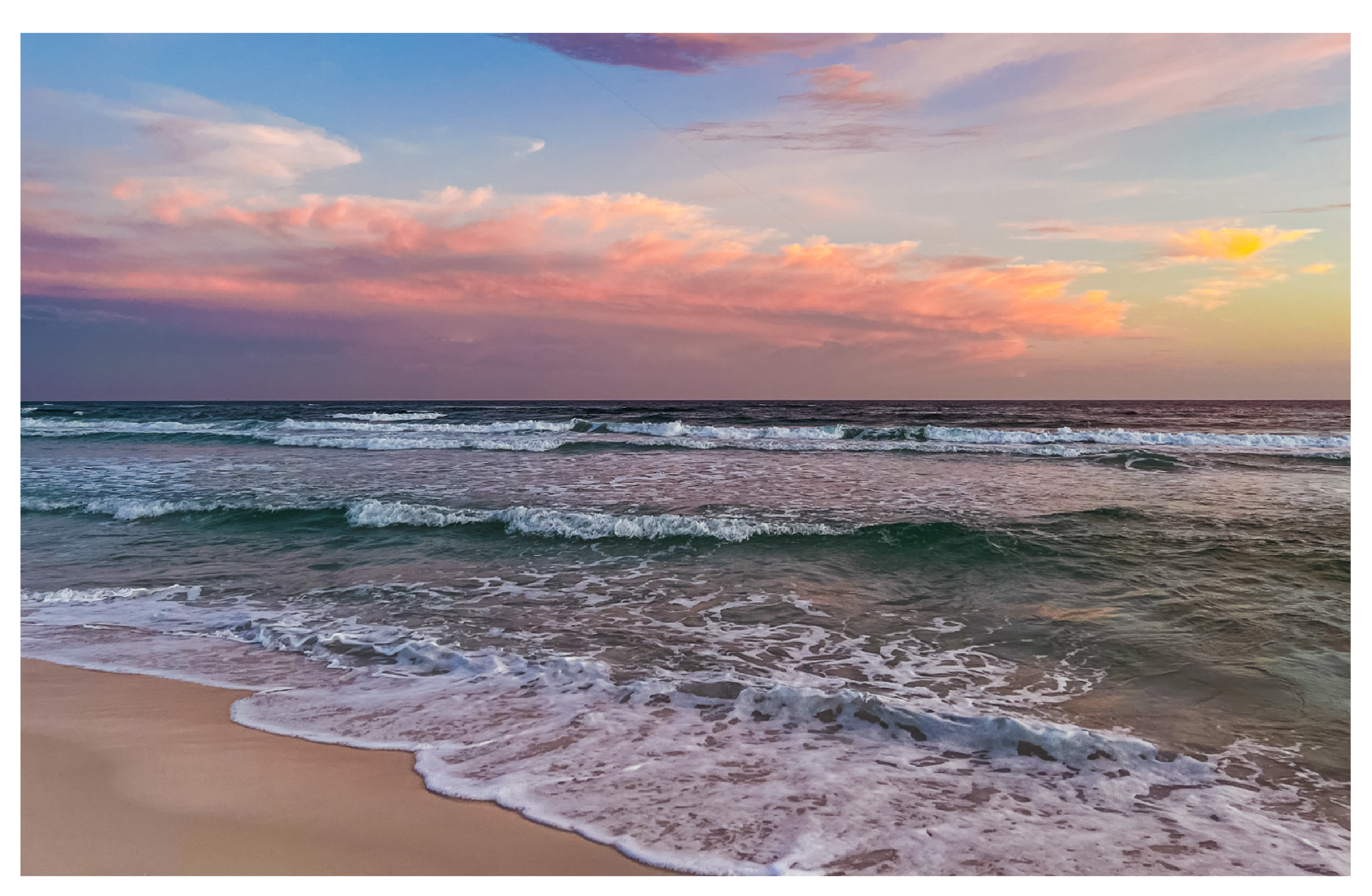 A beach with gentle waves lapping at the shore during sunset, with colorful pink and orange clouds in the sky.