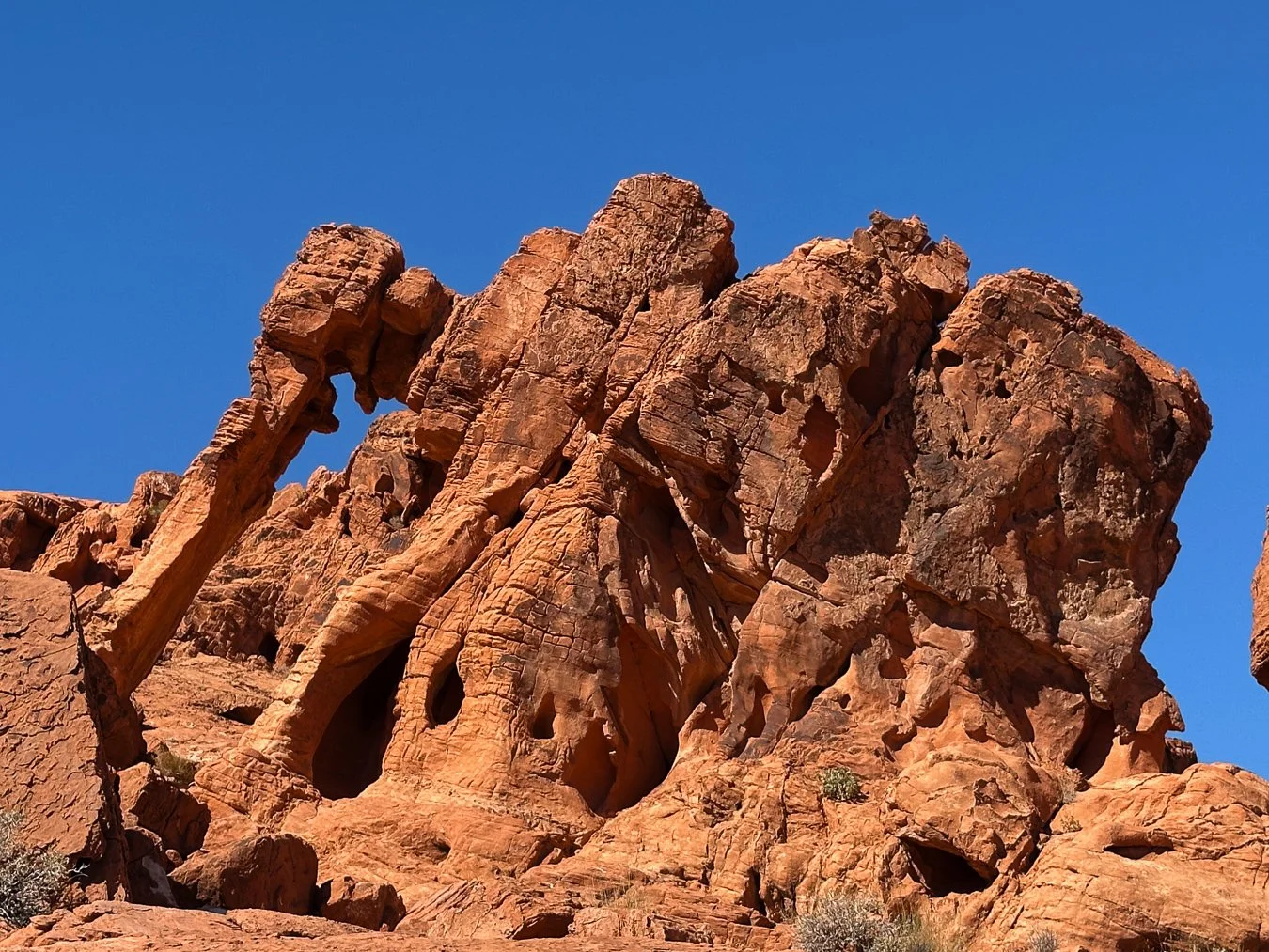 Close-up of a large rock formation with reddish-brown hues against a clear blue sky.