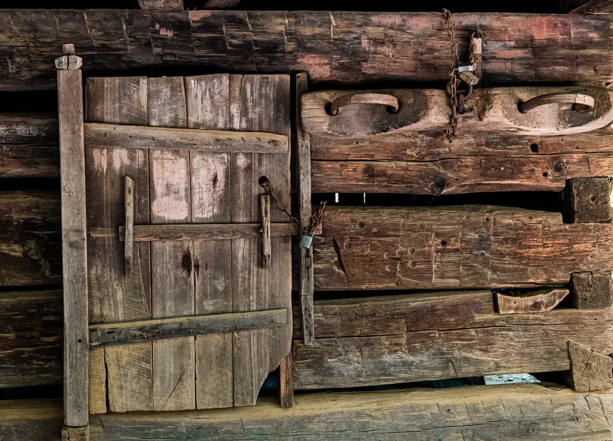 Old wooden barn door with a latch and chains, surrounded by weathered wooden planks.