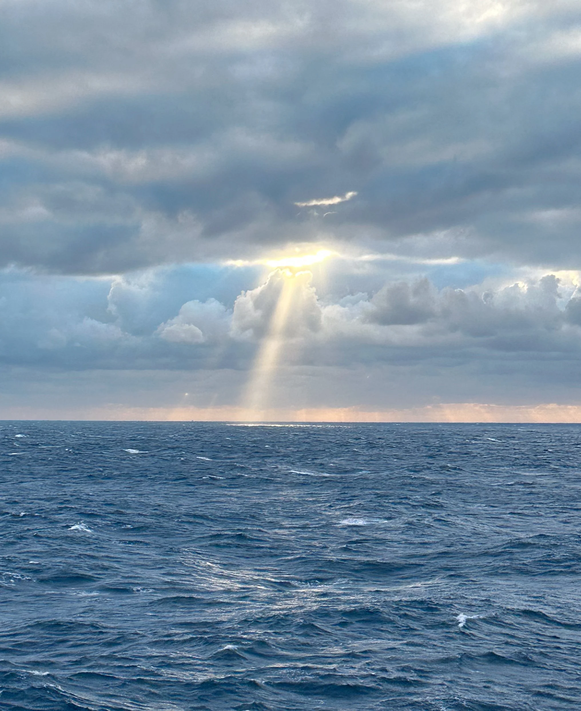 Sunshine breaking through clouds over the ocean with waves.