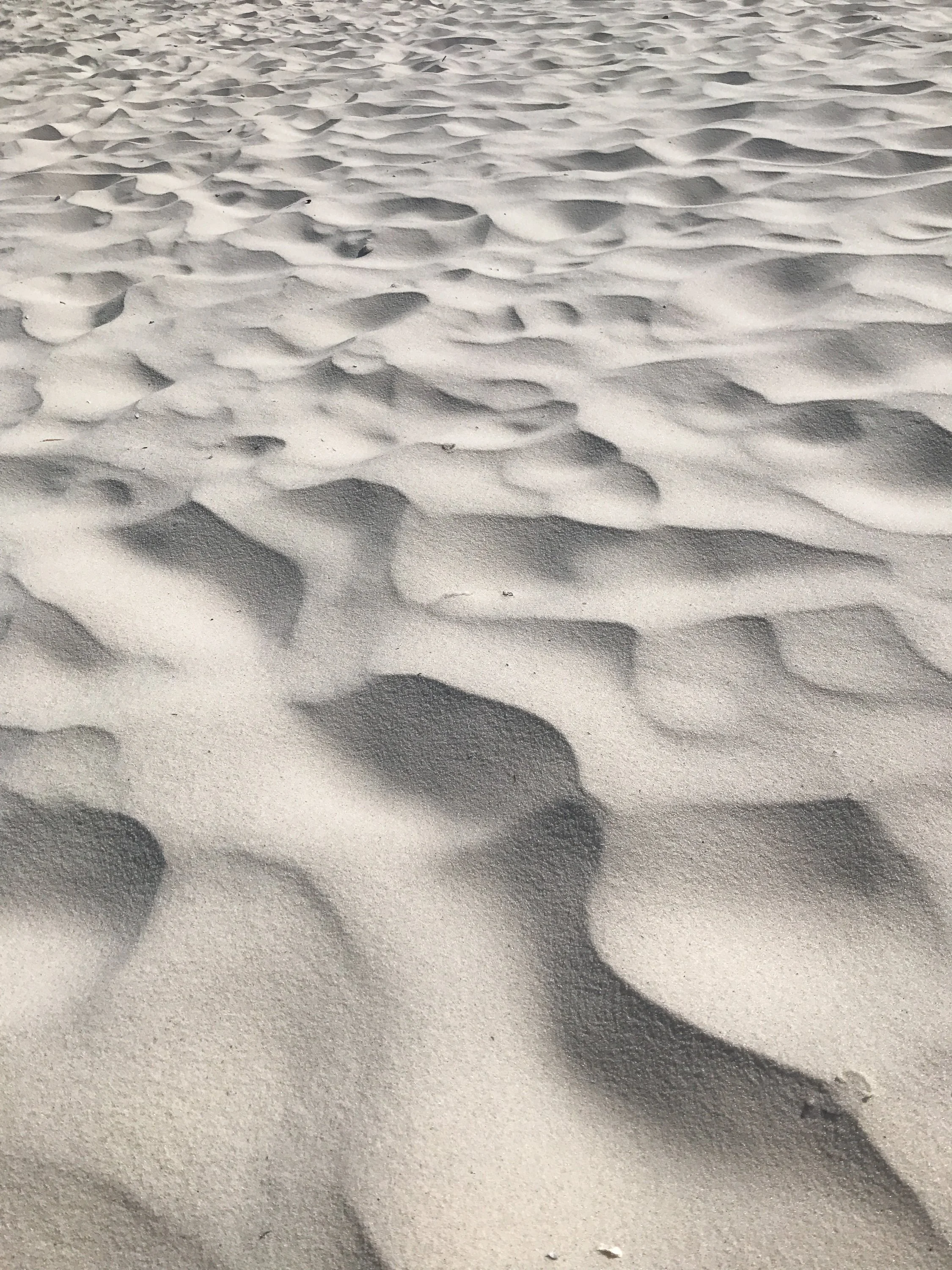 Close-up view of white sand with wind-blown lines and shadows at a beach.