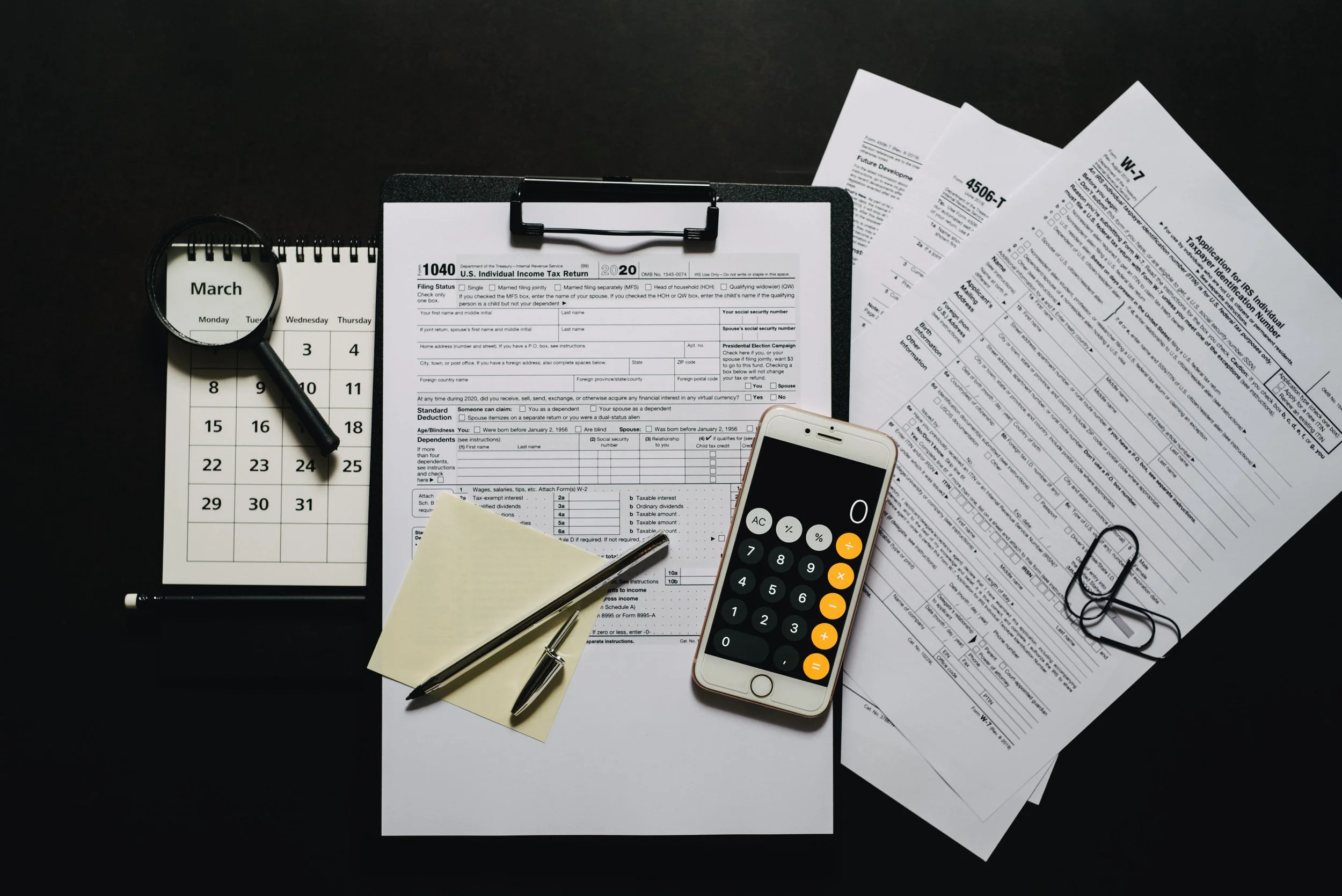 Desk with financial documents, a calendar, a magnifying glass, a pen, and a smartphone.
