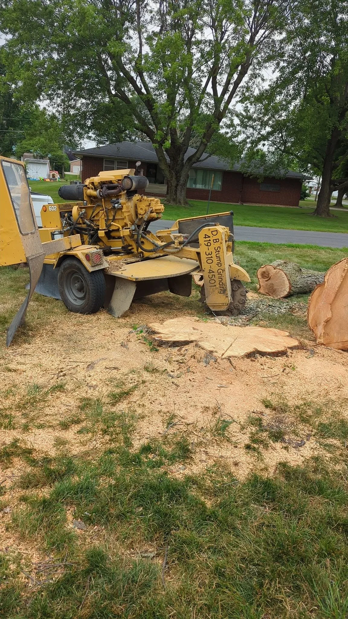A wood planer cutter machine cutting a log into slabs on a grassy lawn.