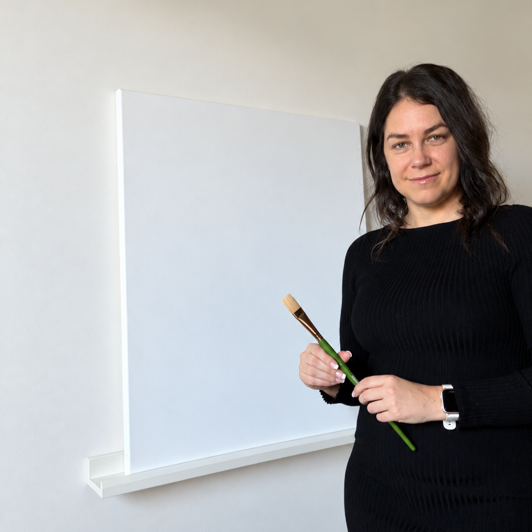 Une femme tient un pinceau dans une salle avec un tableau blanc derrière.