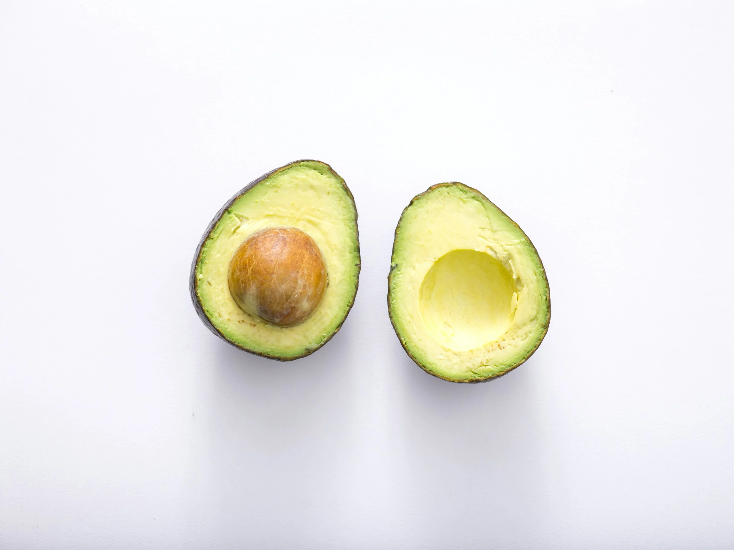 Halved avocado with seed on a white surface.