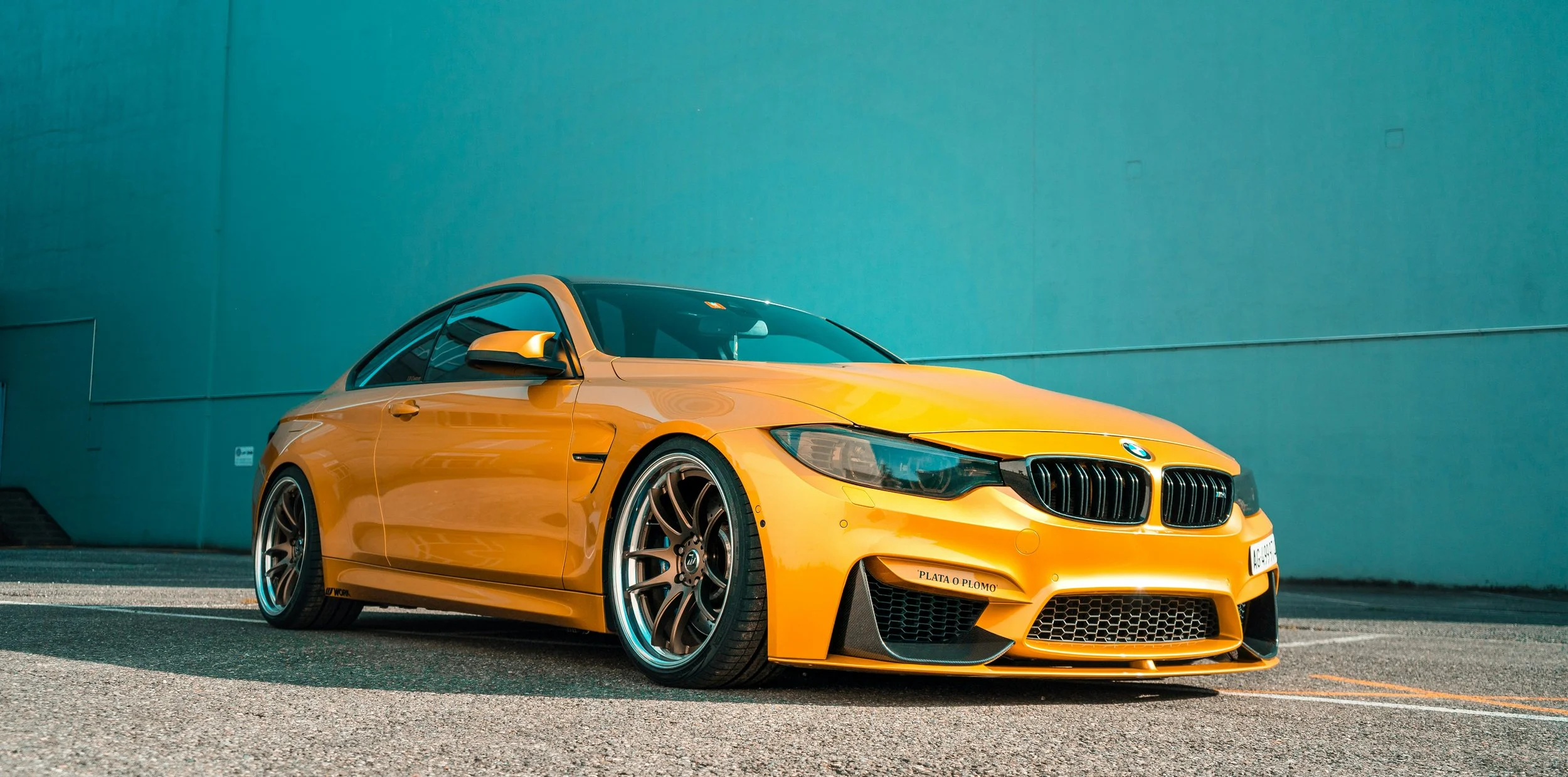 A yellow BMW sports car parked against a teal-colored wall.