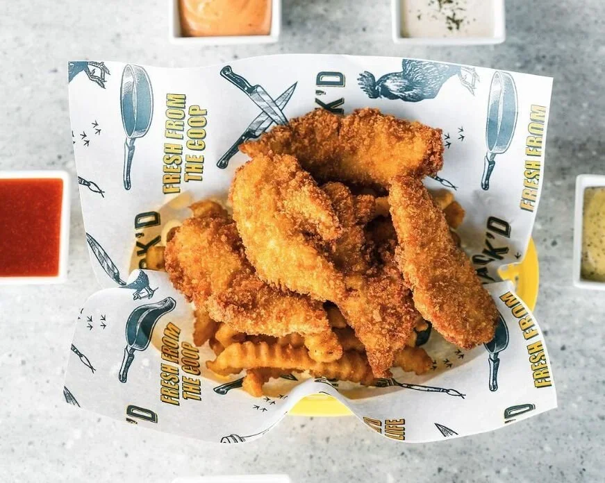 Fried fish fillets in a basket with a sheet of branded paper, served with waffle fries, surrounded by small bowls of dipping sauces.