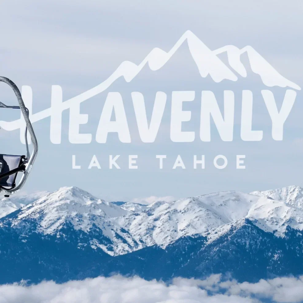 Snow-covered mountains and a cloudy sky with the text 'Heavenly Lake Tahoe' and a ski lift in the foreground.