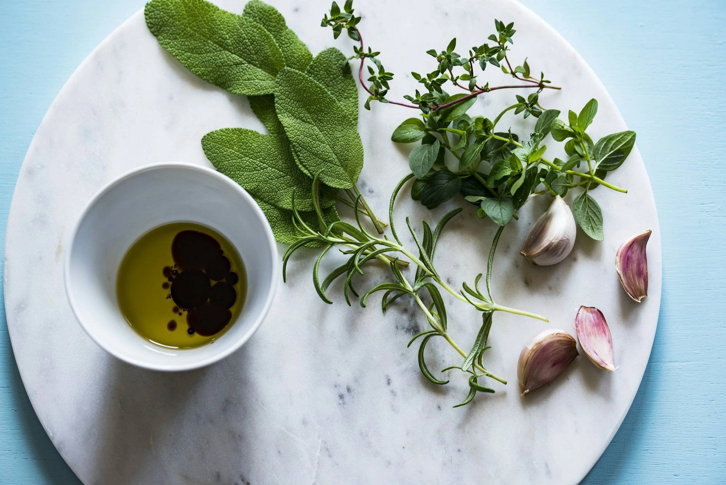 Fresh herbs, garlic, and olive oil on a white marble board