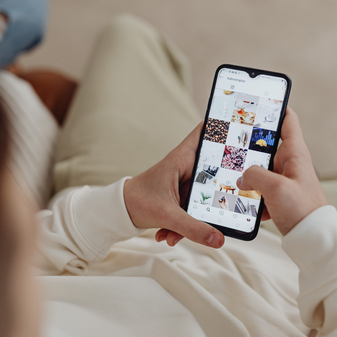 Hands holding a phone showing a grid of social media photos