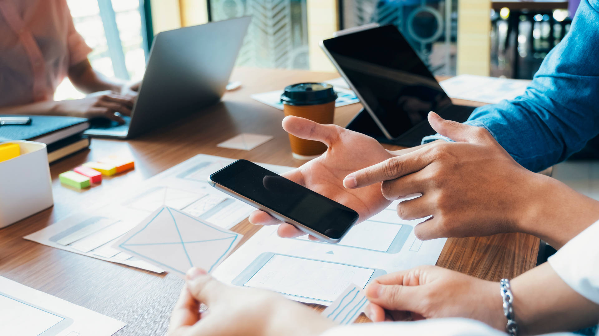 Hands holding a phone with designs laid out on a conference table