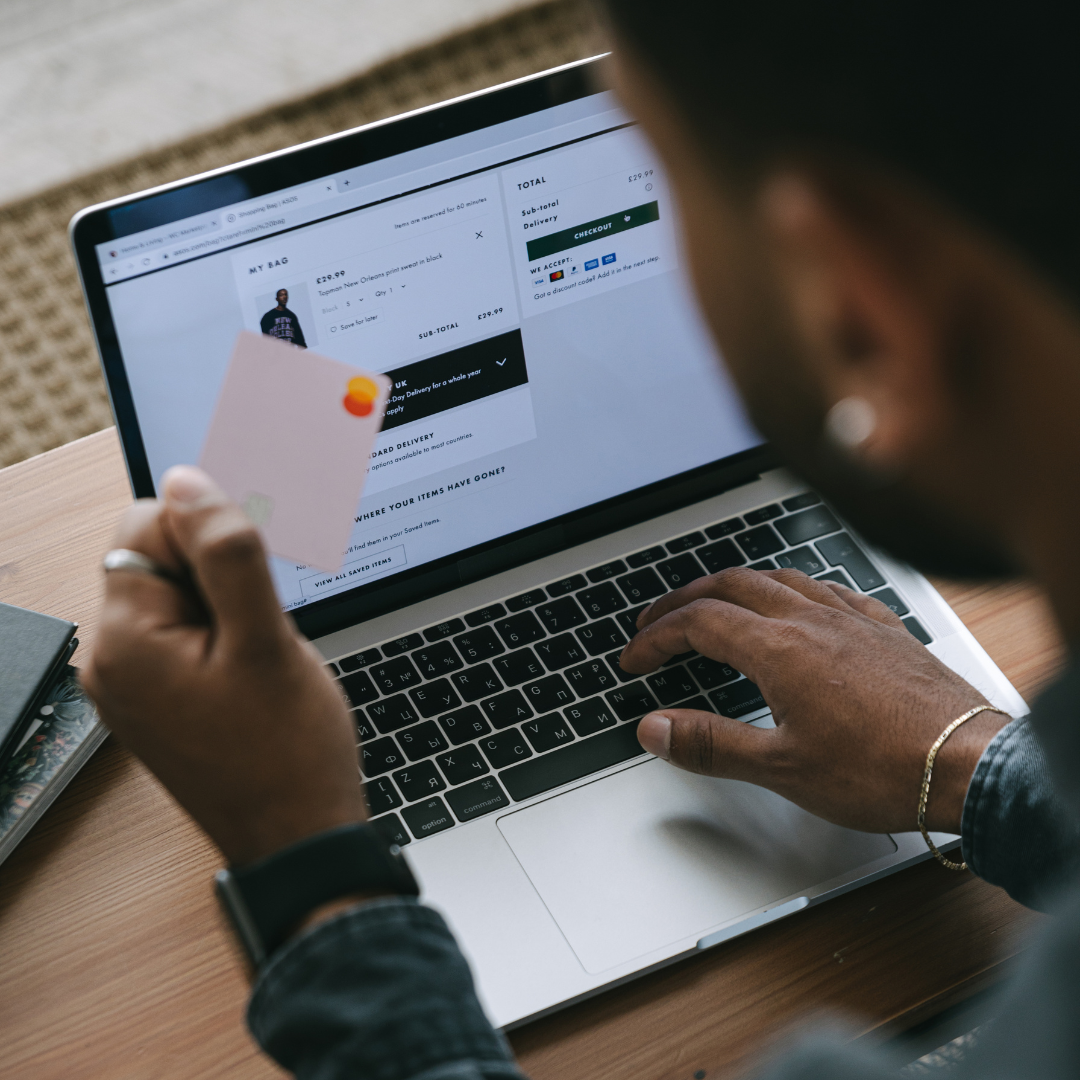 Person shopping online on a laptop, holding a credit card, with a browser window showing an online shopping cart and checkout page.