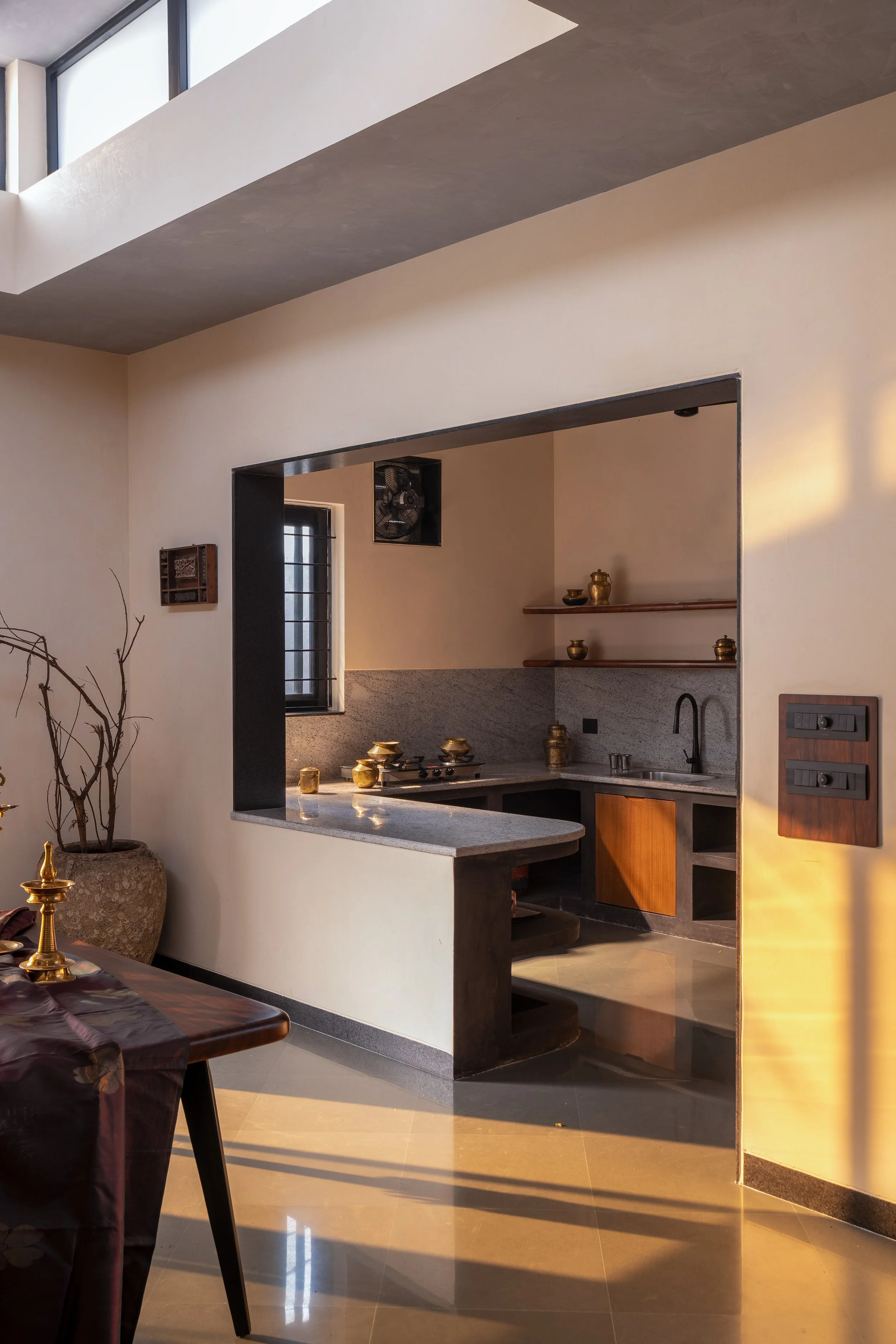 A modern kitchen with a beige wall, open shelves with decorative containers, grey and wood cabinetry, a granite countertop, a black faucet, and a window allowing natural light to enter.