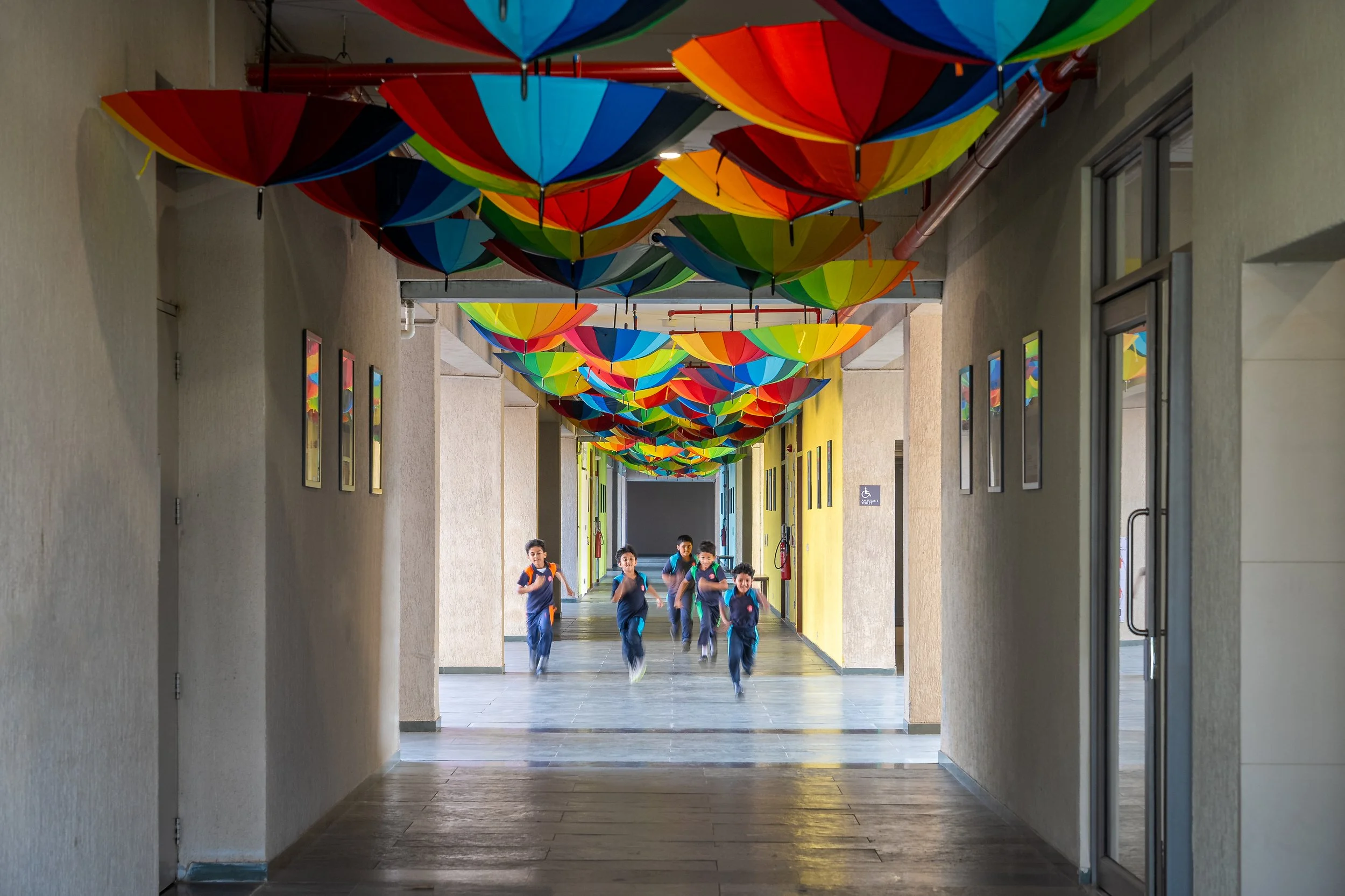 Children running down a school corridor decorated with colorful umbrellas hanging from the ceiling.