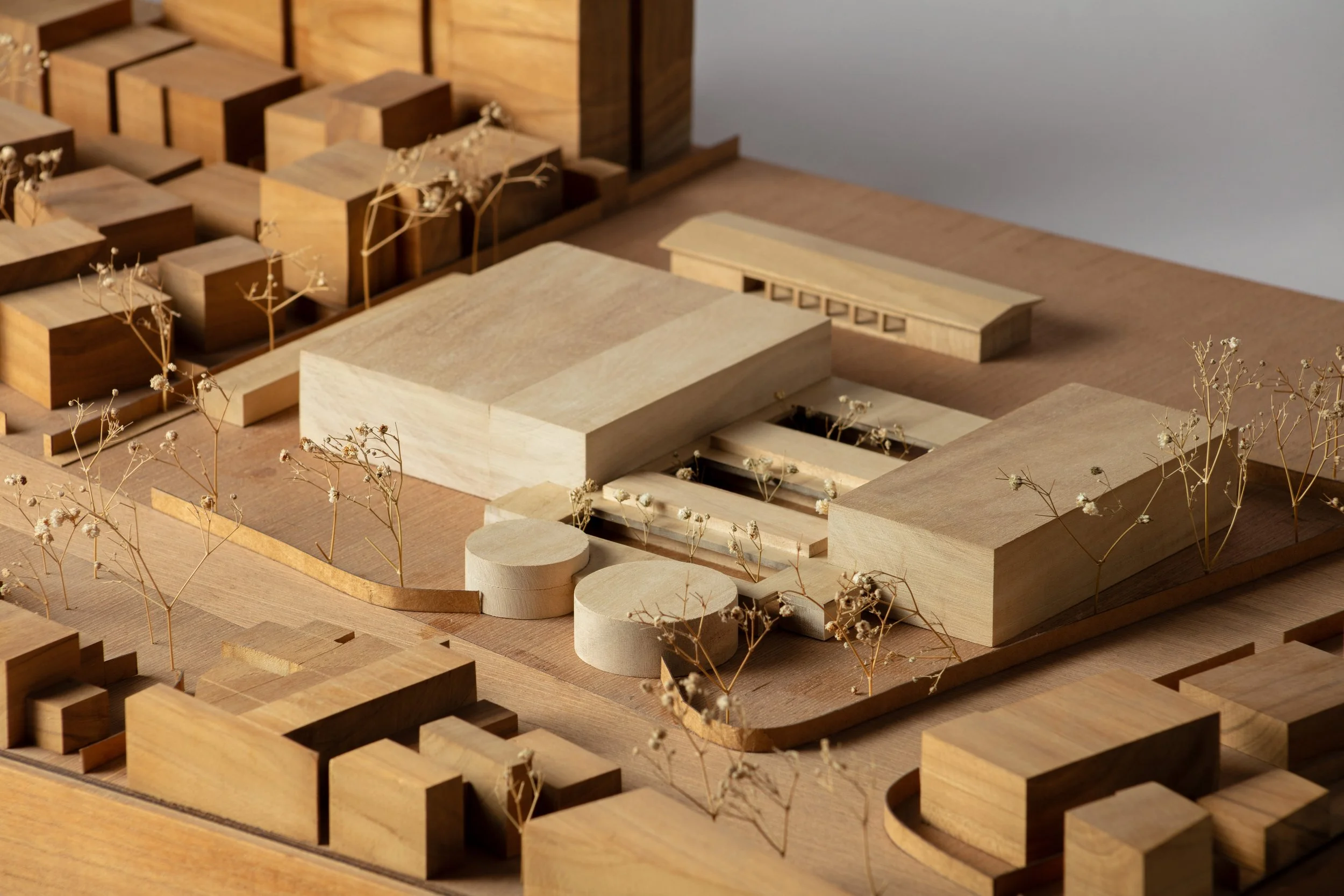 A detailed architectural model made of wood, showing a planned urban development with multiple buildings, open spaces, and small trees.