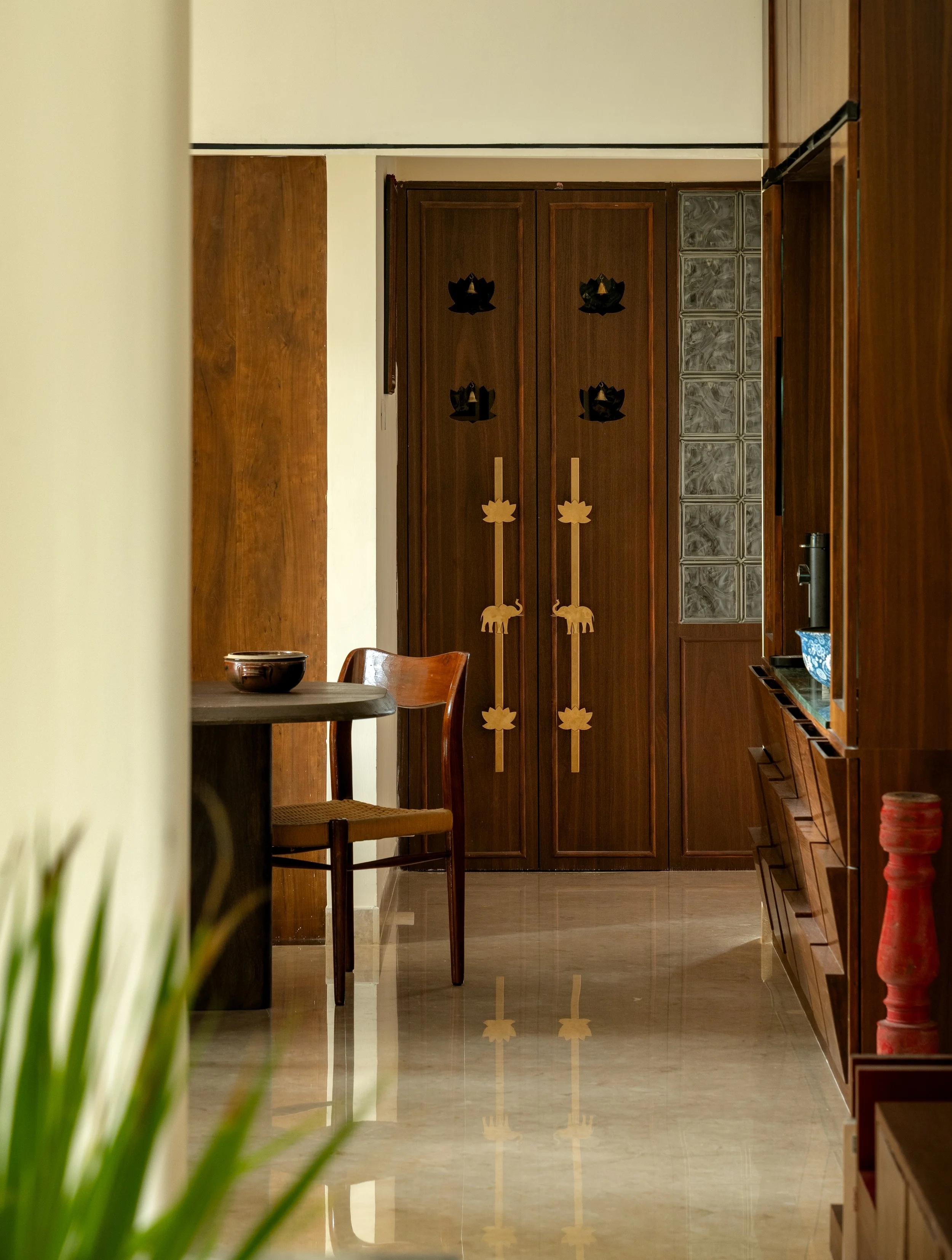 Interior hallway with wooden furniture, glass block wall on the right, a wooden door with decorative elements in the center, and a reflecting polished floor.