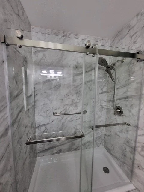 Marble shower with sliding glass door and handheld showerhead.