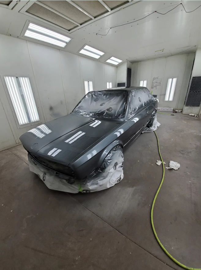 A black car in a paint booth covered with masking paper, ready for painting or drying.