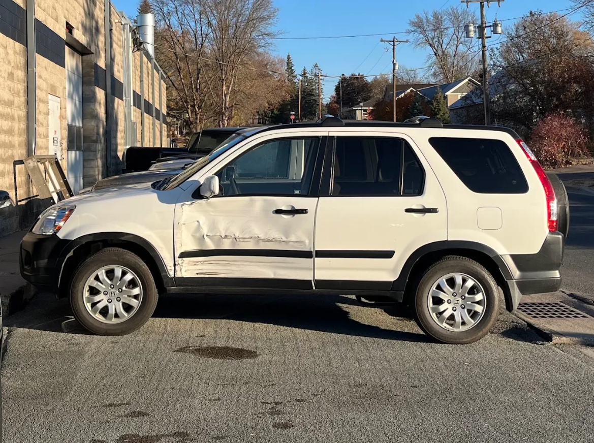 A white SUV with a dented driver side door parked on the street.