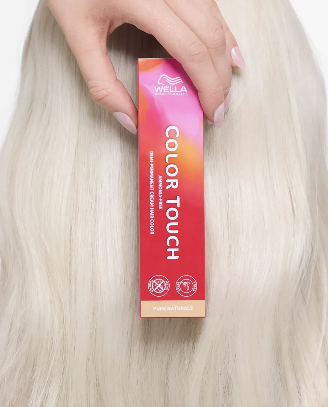 A hand holding a small box of Wella Professionals Color Touch demi-permanent cream hair color against a blonde hair background.