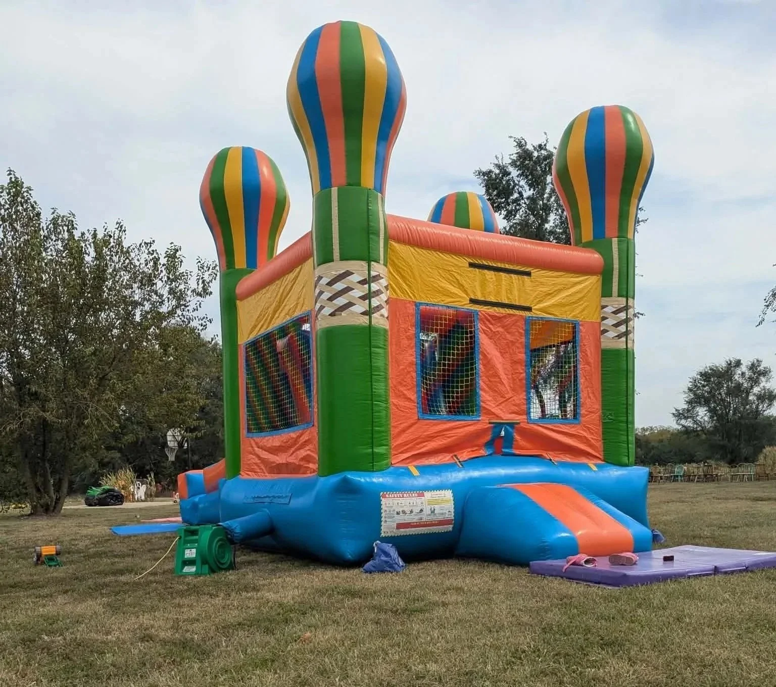 Colorful inflatable bounce house with striped hot air balloon design and mesh windows, set up outdoors on grass.